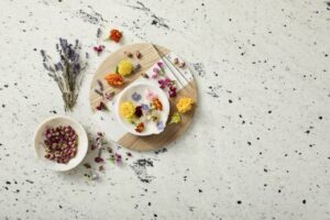 A bowl of multi-color floral infusions sits on top of a circular cutting board. Nearby is a bowl of more floral infusions.