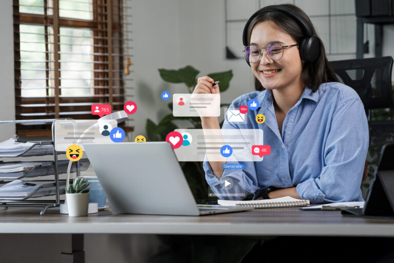 A woman wearing glasses and headphones sits at a table using a laptop. Floating between her and the laptop are icons showing social media posts and post reactions such as “like” or “heart” emojis.