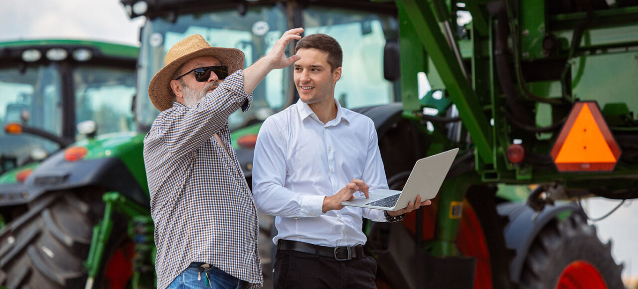 Farmer and marketing professional standing in front of a tractor